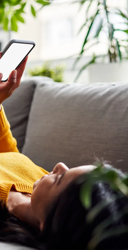 Frau liegt mit Smartphone in der Hand auf der Couch.