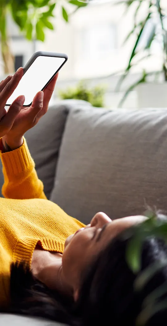 Frau liegt mit Smartphone in der Hand auf der Couch. 