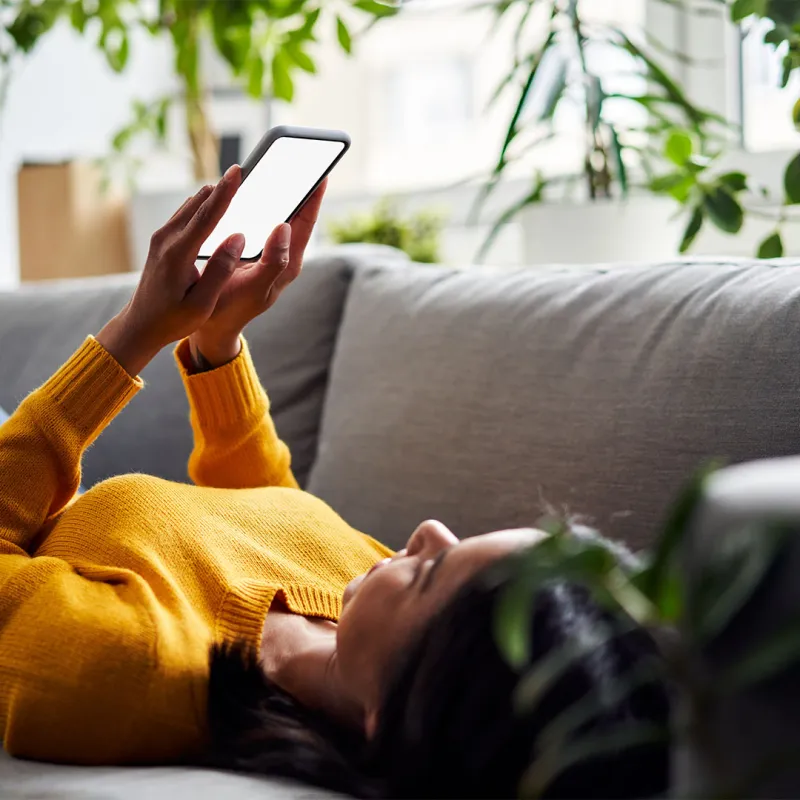 Frau liegt mit Smartphone in der Hand auf der Couch. 